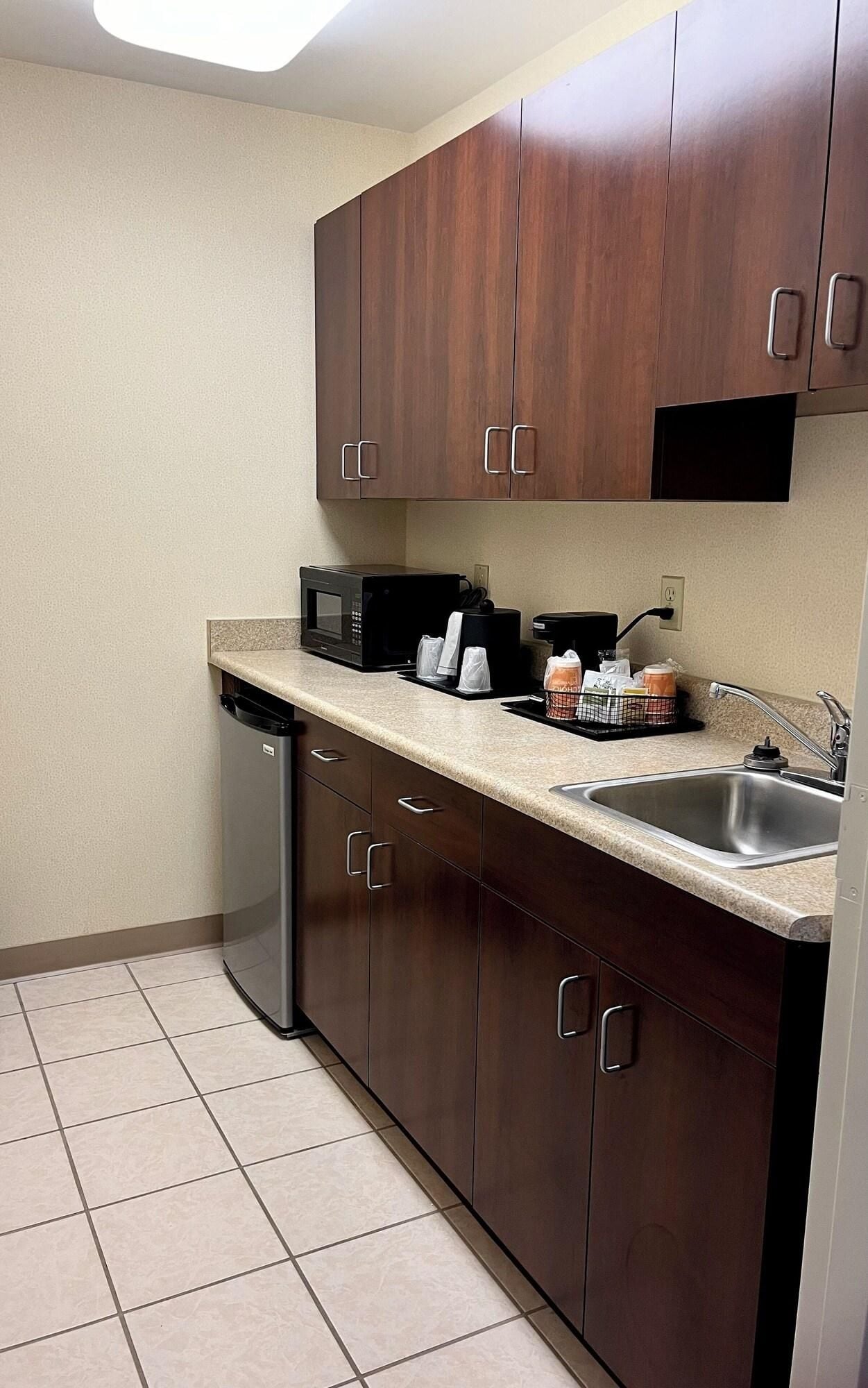 Cocina compacta con armarios de madera oscura, pileta de acero inoxidable, lavavajillas, microondas y cafetera.
