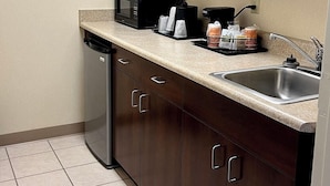 A compact kitchen with dark wooden cabinets, a stainless steel sink, a dishwasher, a microwave, and a coffee maker. - Quality Inn & Suites Prestonsburg (Prestonsburg)
