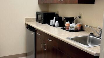 Cocina compacta con armarios de madera oscura, pileta de acero inoxidable, lavavajillas, microondas y cafetera.