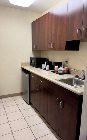 A compact kitchen with dark wooden cabinets, a stainless steel sink, a dishwasher, a microwave, and a coffee maker.
