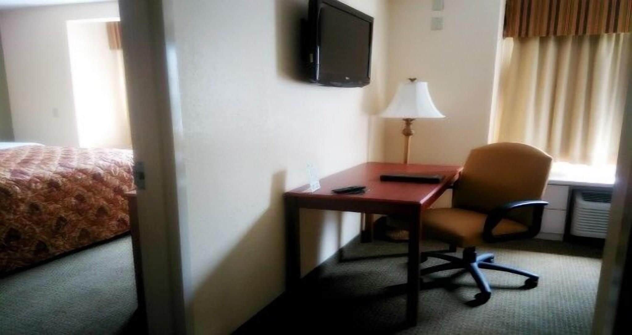 A hotel room with a bed, a desk, a chair, a lamp, a TV, and a window with curtains.