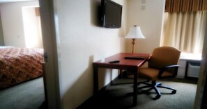 A hotel room with a bed, a desk, a chair, a lamp, a TV, and a window with curtains. - Quality Inn & Suites Prestonsburg (Prestonsburg)