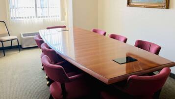 A conference room with a long table, six chairs, a single chair, a radiator, and a window with blinds.