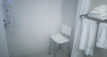 Un baño con ducha, una silla blanca y un perchero con toallas dobladas.