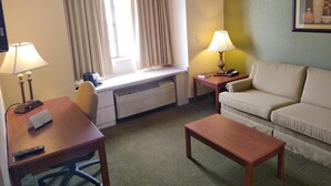 A hotel room with a desk, two lamps, a couch, a window with curtains, and a painting on the wall. - Quality Inn & Suites Prestonsburg (Prestonsburg)