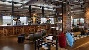 A modern bar with a brick wall, wooden furniture, and a variety of seating options. - Moxy Charleston Downtown (Charleston)