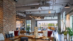 A modern interior with exposed brick walls, wooden furniture, and large windows offering a view of the city. - Moxy Charleston Downtown (Charleston)