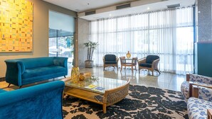 A spacious lobby with a blue sofa, wicker chairs, a glass coffee table, and a large window with sheer curtains. - Flat na Ilha do Leite, Recife 1 quarto. Conforto e Excelente localização OTH1205 (Recife)