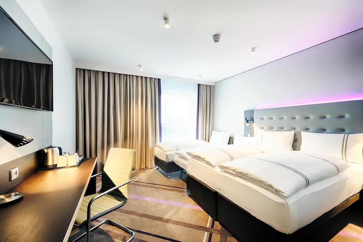 A modern hotel room with a large bed, a desk with a chair, a flat-screen TV, and a large window with curtains.