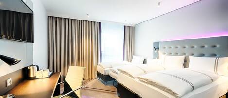 A modern hotel room with a large bed, a desk with a chair, a flat-screen TV, and a large window with curtains.