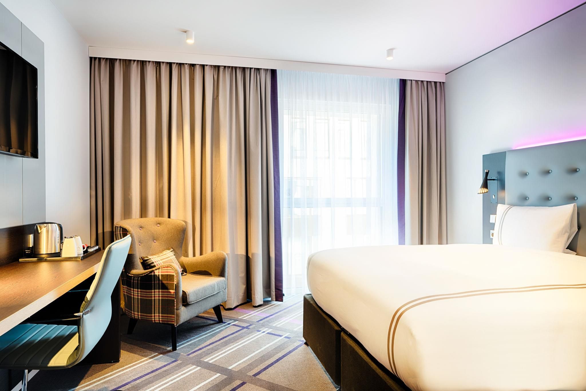 Una habitación de hotel con cama, escritorio, silla, televisor y cortinas.