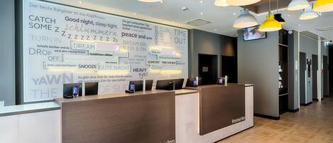 Una recepción de hotel con una gran pared de palabras y frases, un diseño moderno con iluminación colgante y un piso limpio y pulido.