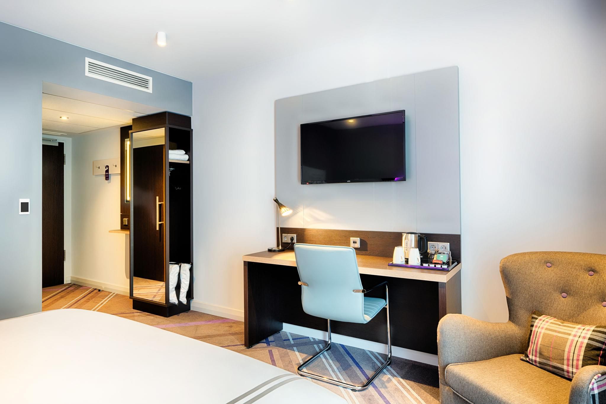 A hotel room with a bed, a desk with a chair, a television, and a wardrobe.