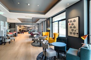 Un moderno vestíbulo de hotel con zonas de estar, una escalera y grandes ventanales.