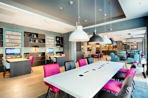 Una sala de conferencias moderna con una gran mesa, varias sillas y una estantería con libros y objetos decorativos.