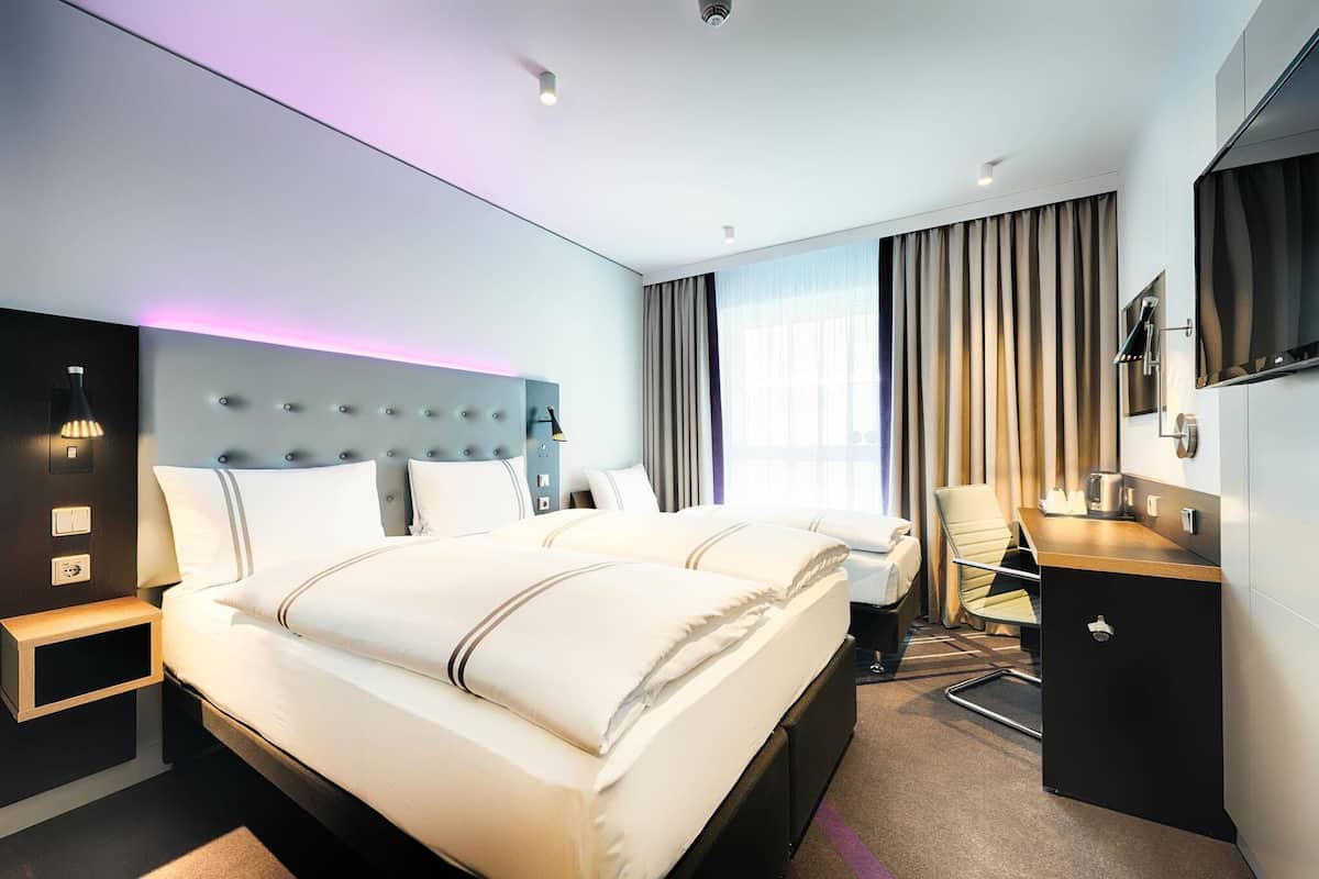 A modern hotel room with a large bed, a desk, a chair, and a TV.