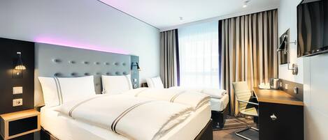 A modern hotel room with a large bed, a desk, a chair, and a TV.