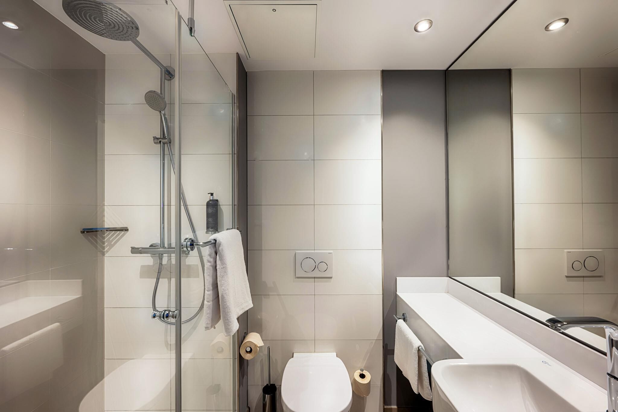 Ein modernes Badezimmer mit Duschkabine aus Glas, einer weißen Toilette und einem großen Spiegel über dem Waschbecken.