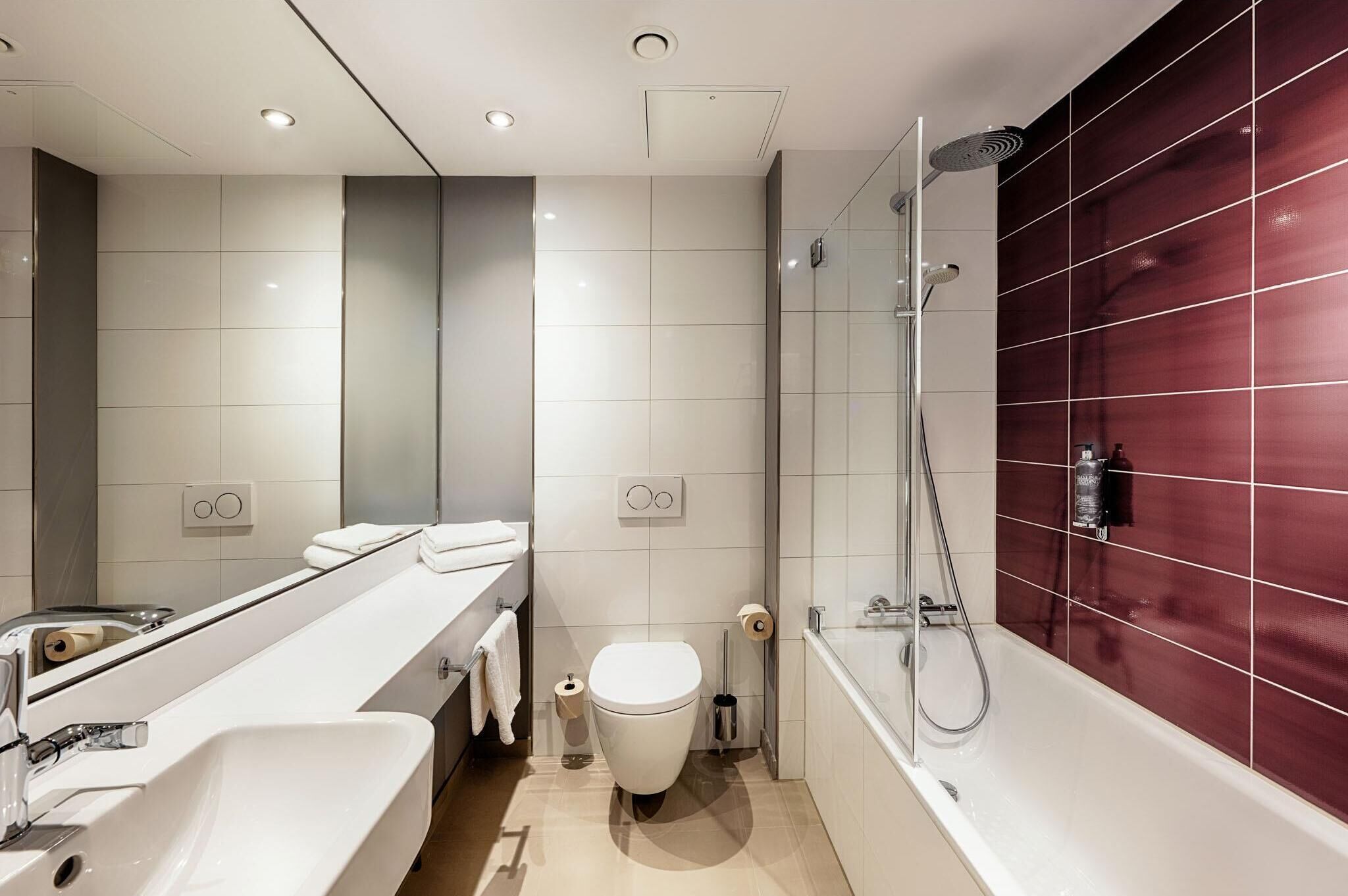 A modern bathroom with a white sink, toilet, and bathtub, and a red-tiled shower area.