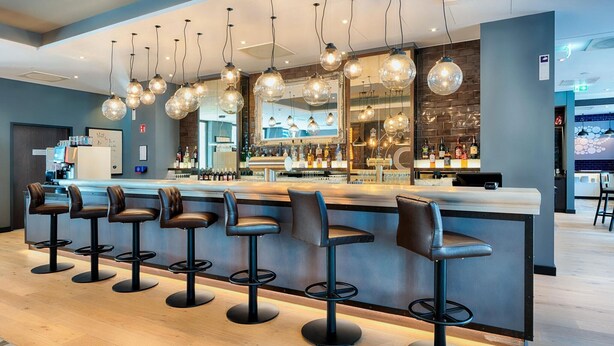 Zona de bar con varios taburetes, una barra y lámparas esféricas colgantes.