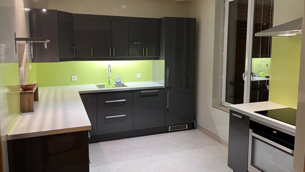 A modern kitchen with dark cabinets, a green backsplash, and a built-in oven. - Air-conditioned house near RER / Paris / Disney / CDG (Gagny)