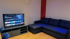 A modern living room with a flat-screen TV, a dark blue sofa, and a wooden floor. - Air-conditioned house near RER / Paris / Disney / CDG (Gagny)