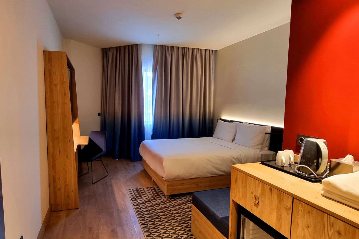 Una habitación de hotel con cama, escritorio, cafetera y una pared roja decorativa.