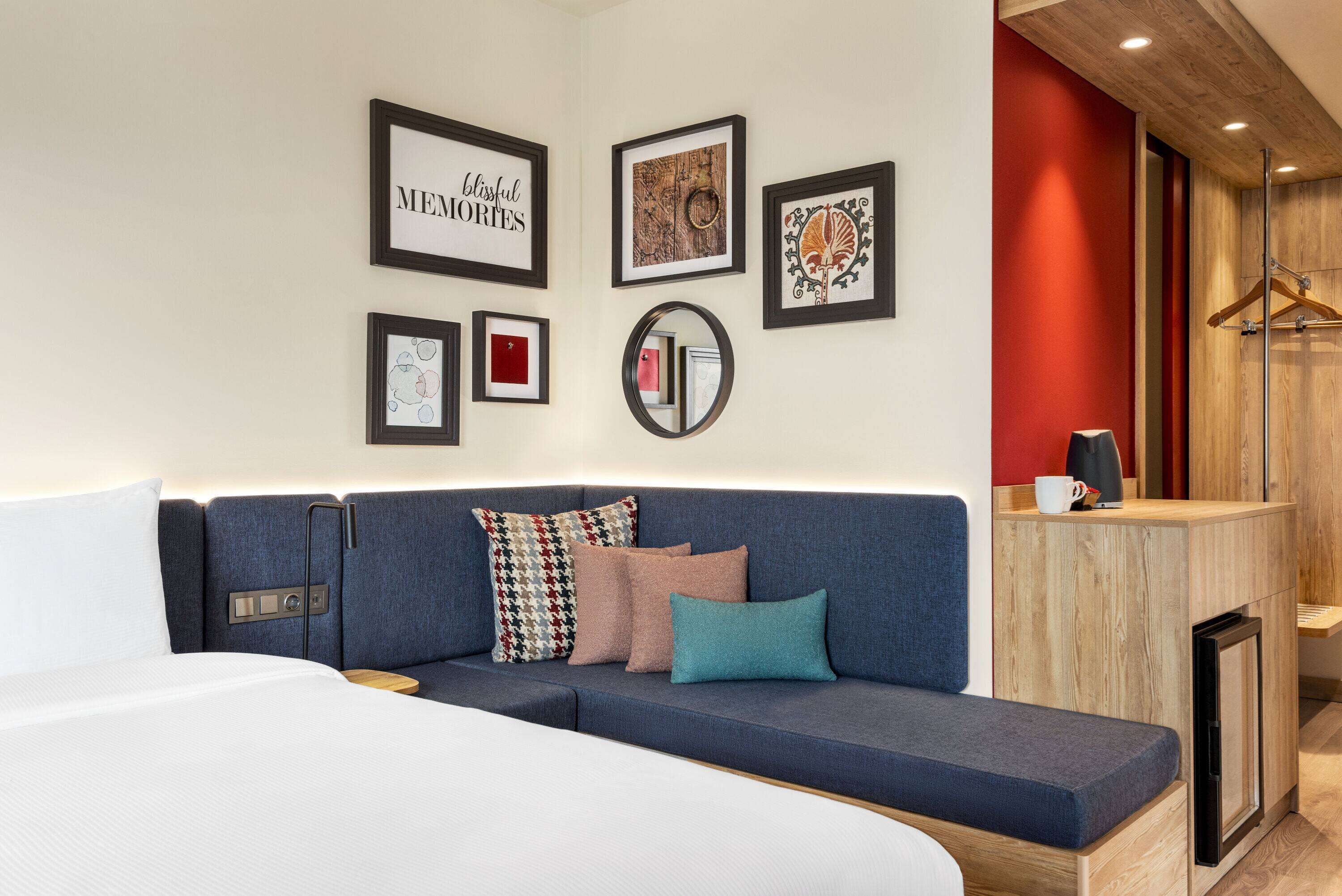 A modern hotel room with a sofa, a bed, a wooden side table, and a mirror.
