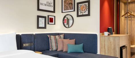 A modern hotel room with a sofa, a bed, a wooden side table, and a mirror.