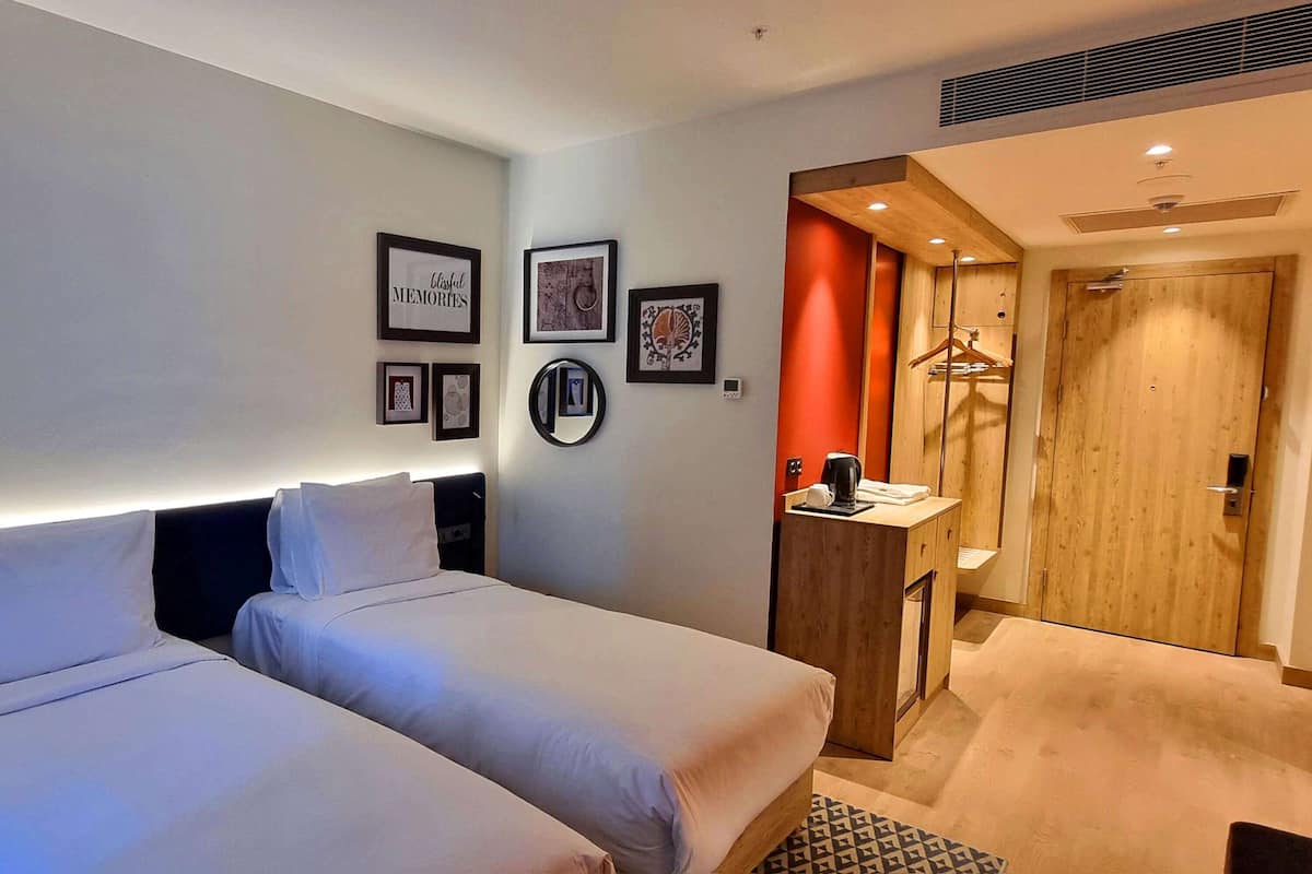 Habitación de hotel con dos camas, un armario de madera, un pequeño escritorio con cafetera y un espejo.