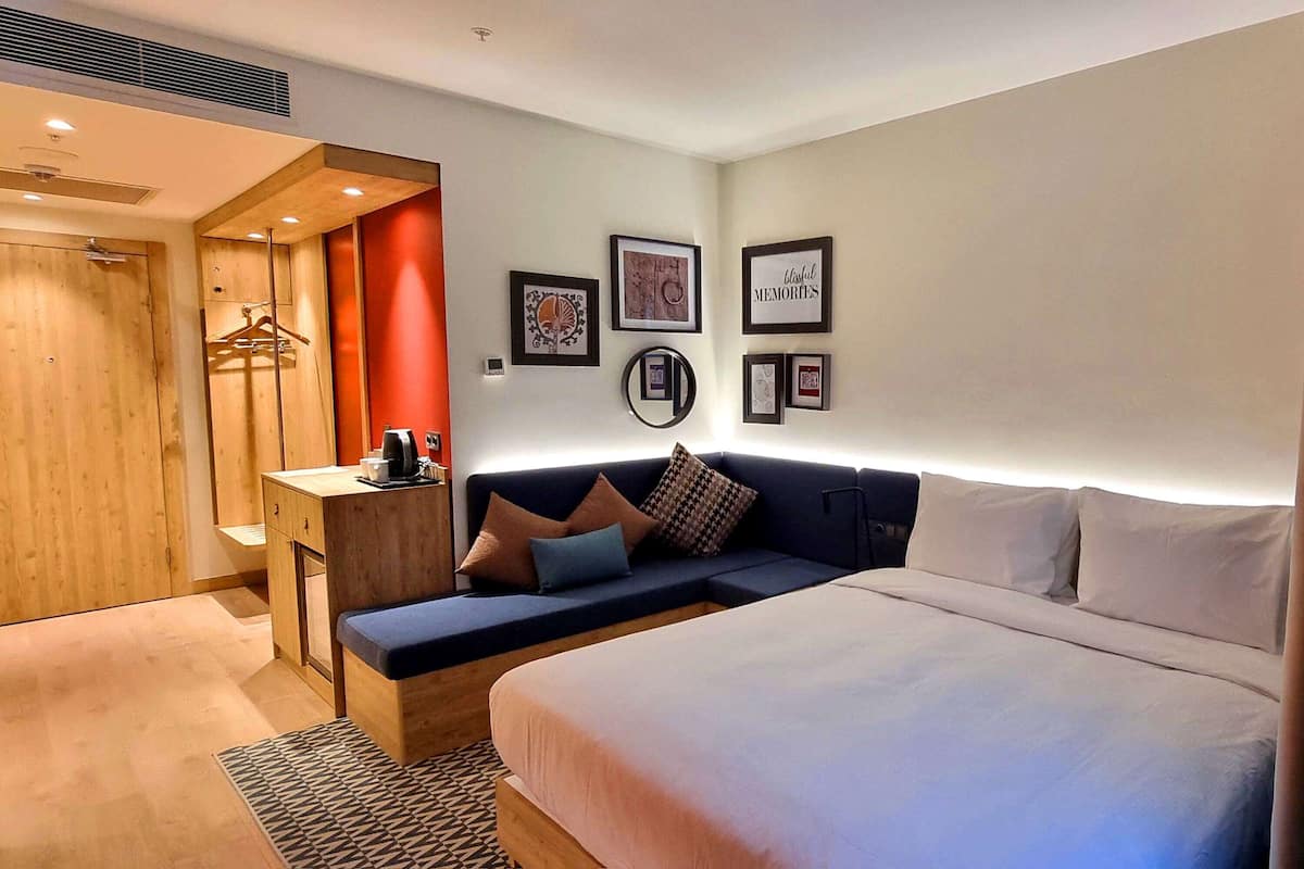 Una habitación de hotel moderna con una cama grande, una zona de estar con cojines, un escritorio de madera y un armario.