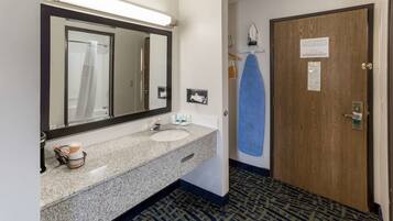 A hotel bathroom with a granite sink, a mirror, a towel rack, and a door with a sign.