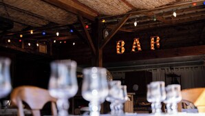 Ein rustikaler Innenraum mit Holzbalkendecke, einem Schild mit der Aufschrift 'BAR' und mehreren leeren Gläsern auf einem Tisch.