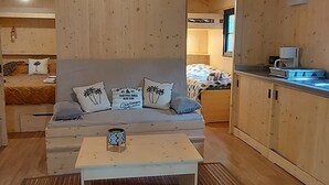 Ein gemütliches Blockhäuschen-Interieur mit Holzboden, einer Couch mit Zierkissen, einem Couchtisch und einer Küchenzeile mit Schränken und einer Arbeitsplatte.