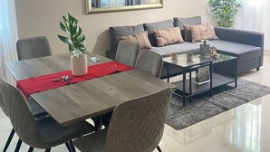 Un salon moderne comprenant un coin repas, un ensemble de canapés, une table basse et une grande fenêtre avec des rideaux.