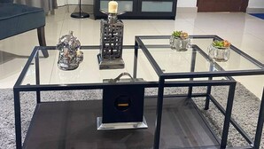 Un salon avec une table basse en verre, un meuble pour la télévision, une lampe et une porte.