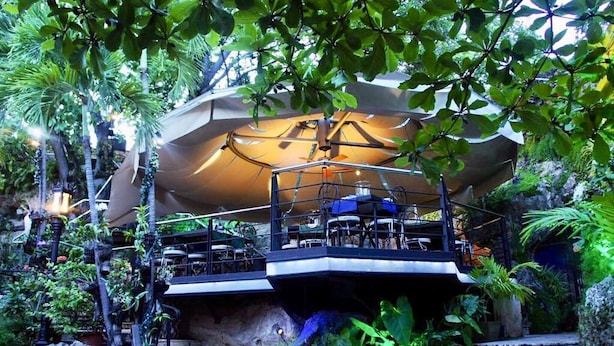 Un restaurant doté d’une terrasse aménagée sur un escalier en pierre, entouré d’une végétation luxuriante et de plantes tropicales.