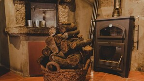 A rustic kitchen with a stone wall, a wooden stove, and a wicker basket filled with firewood. - The Farmhouse I (Porto)