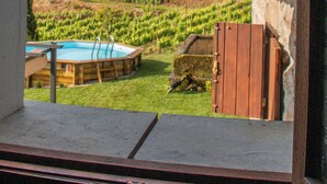A view from a window of a building with a pool, a wooden deck, and a hillside with greenery. - The Farmhouse I (Porto)