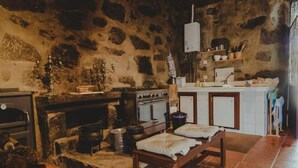 A rustic kitchen with stone walls, a wood-burning stove, a sink, and a wooden bench. - The Farmhouse I (Porto)