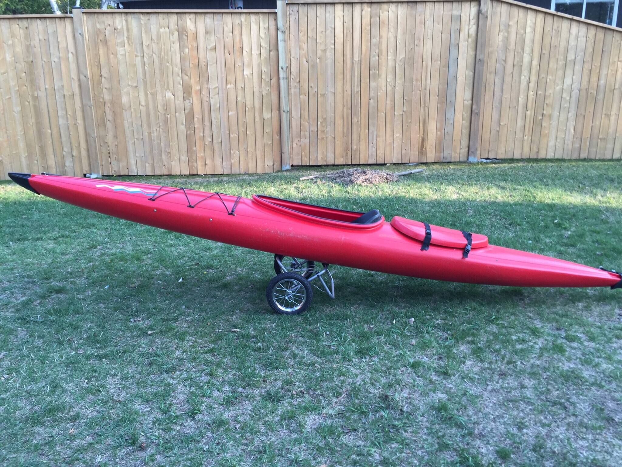 A red kayak on a lawn with a wooden fence in the background.
