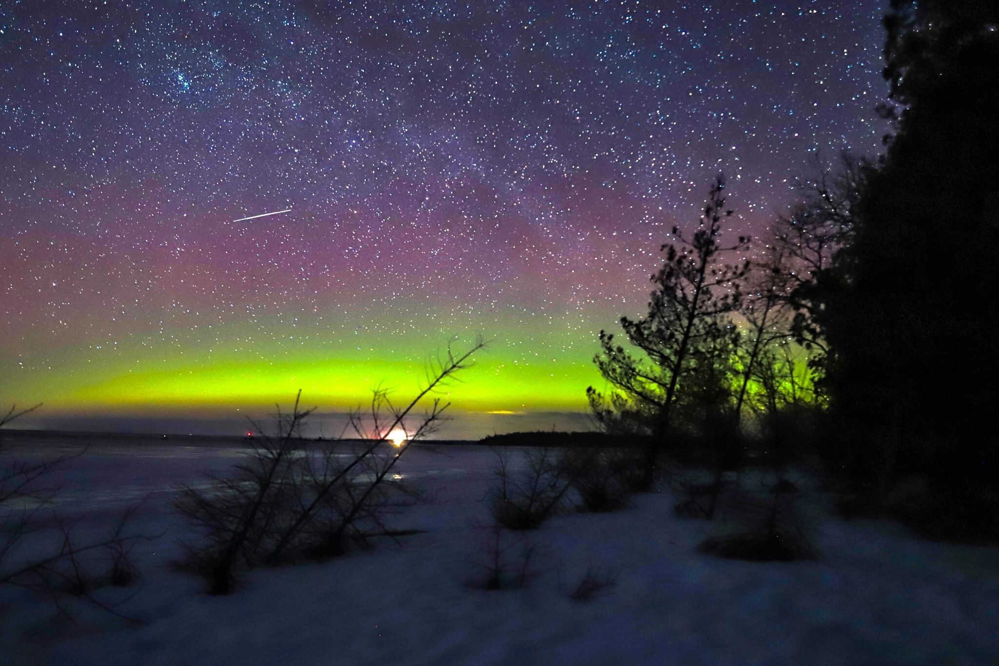 Een heldere sterrenhemel boven een besneeuwd landschap, met een zichtbare aurora.