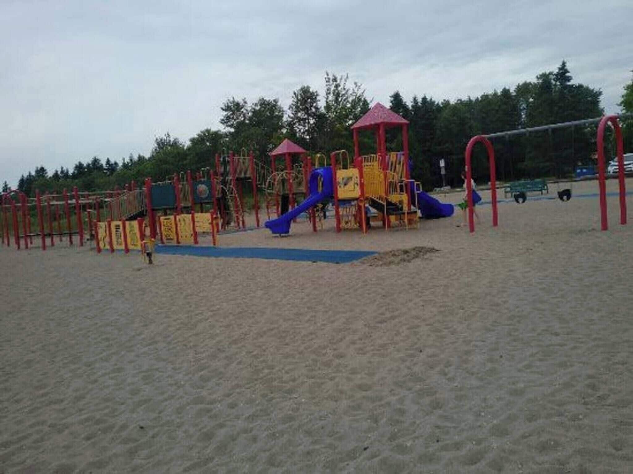 A playground with various play structures, including slides and climbing areas, on a sandy surface.