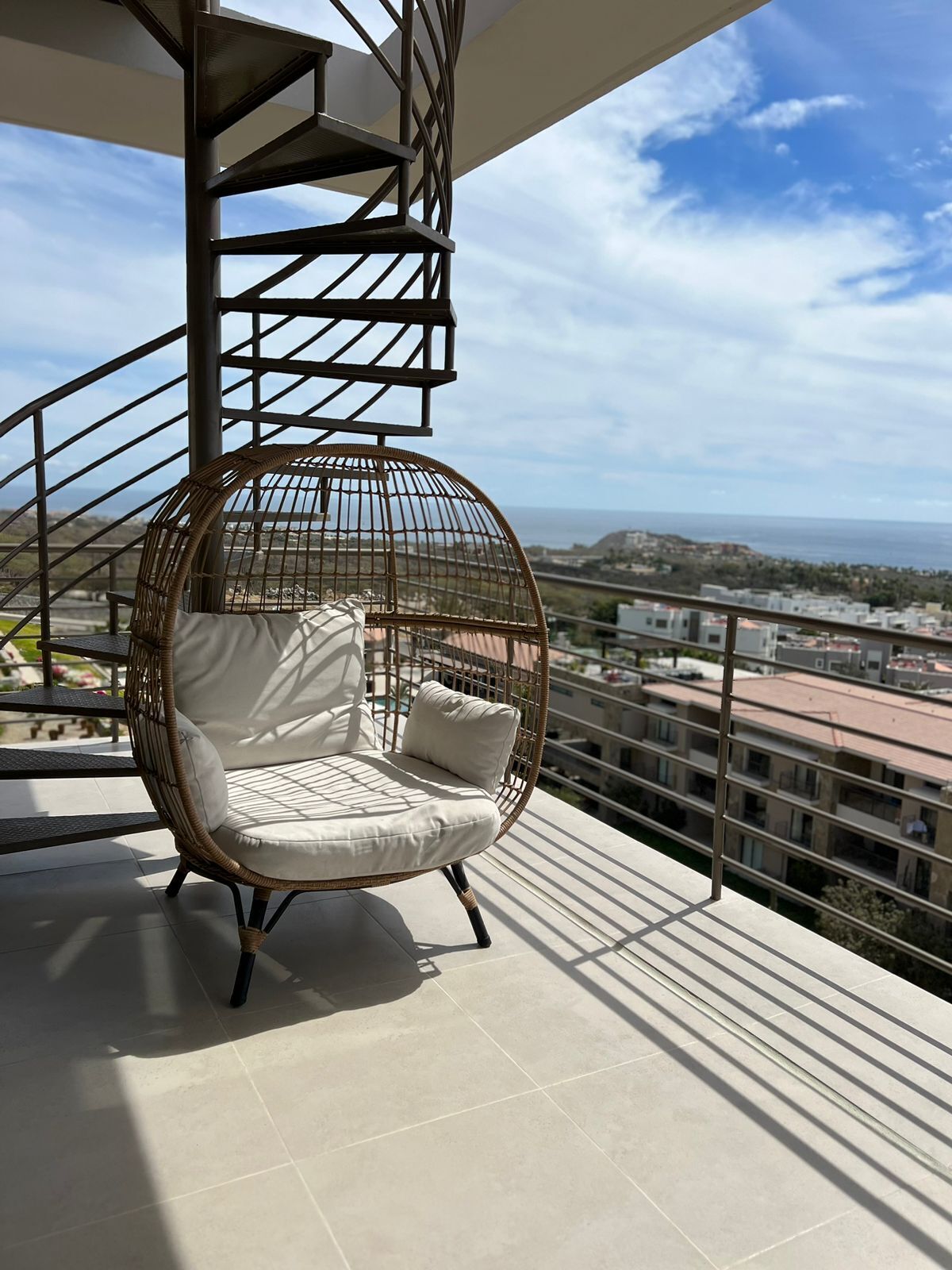 A balcony with a wicker chair and a spiral staircase.