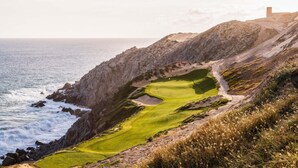 En kystgolfbane med ujævnt terræn, et klart havudsigt og en bygning i det fjerne på en bakke.