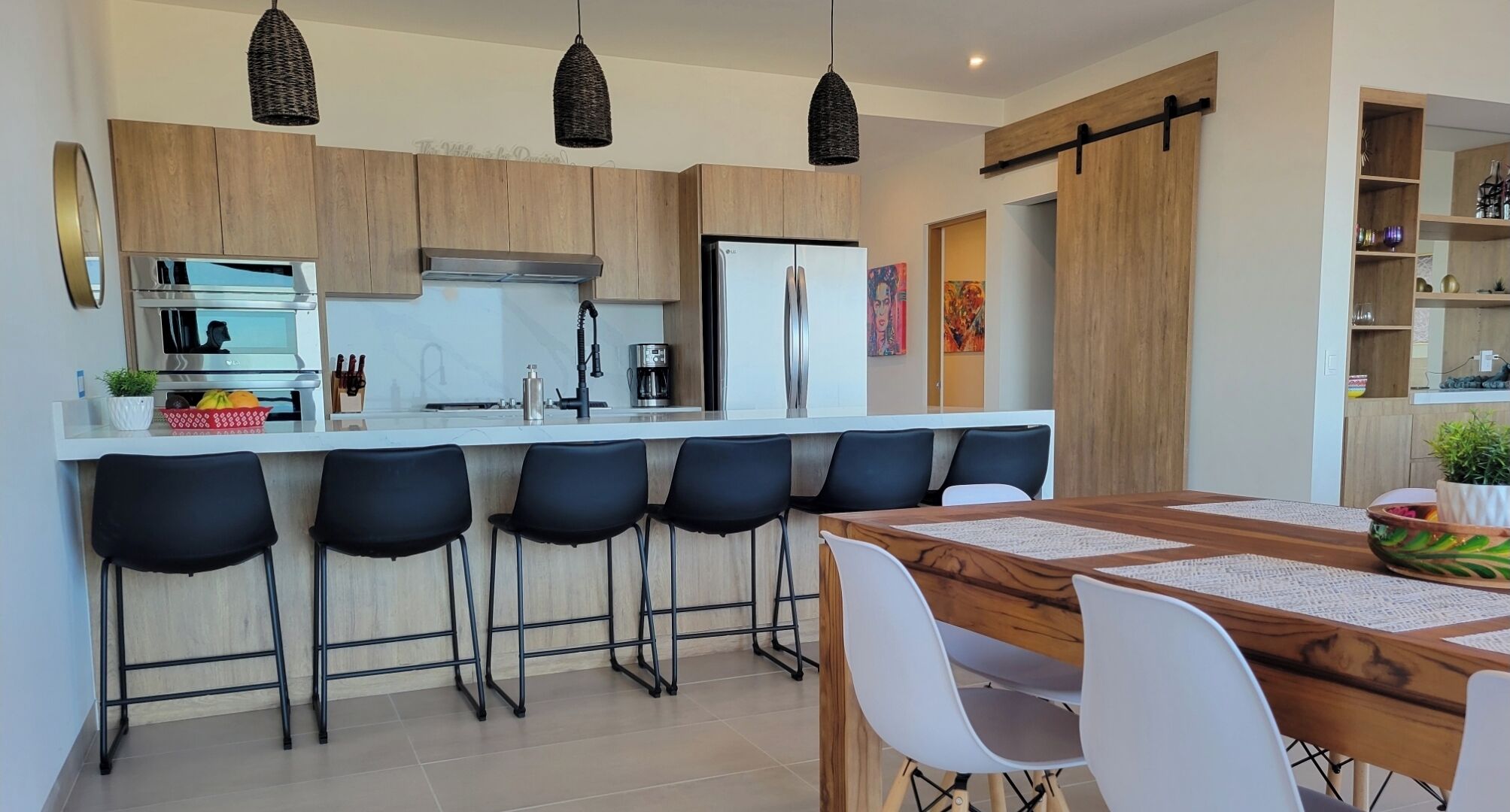 A modern kitchen with wooden cabinets, a white countertop, and black bar stools.