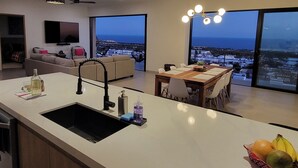 Et moderne køkken med en stor ø, et spiseområde med udsigt og en opholdsstue med sofa og TV.