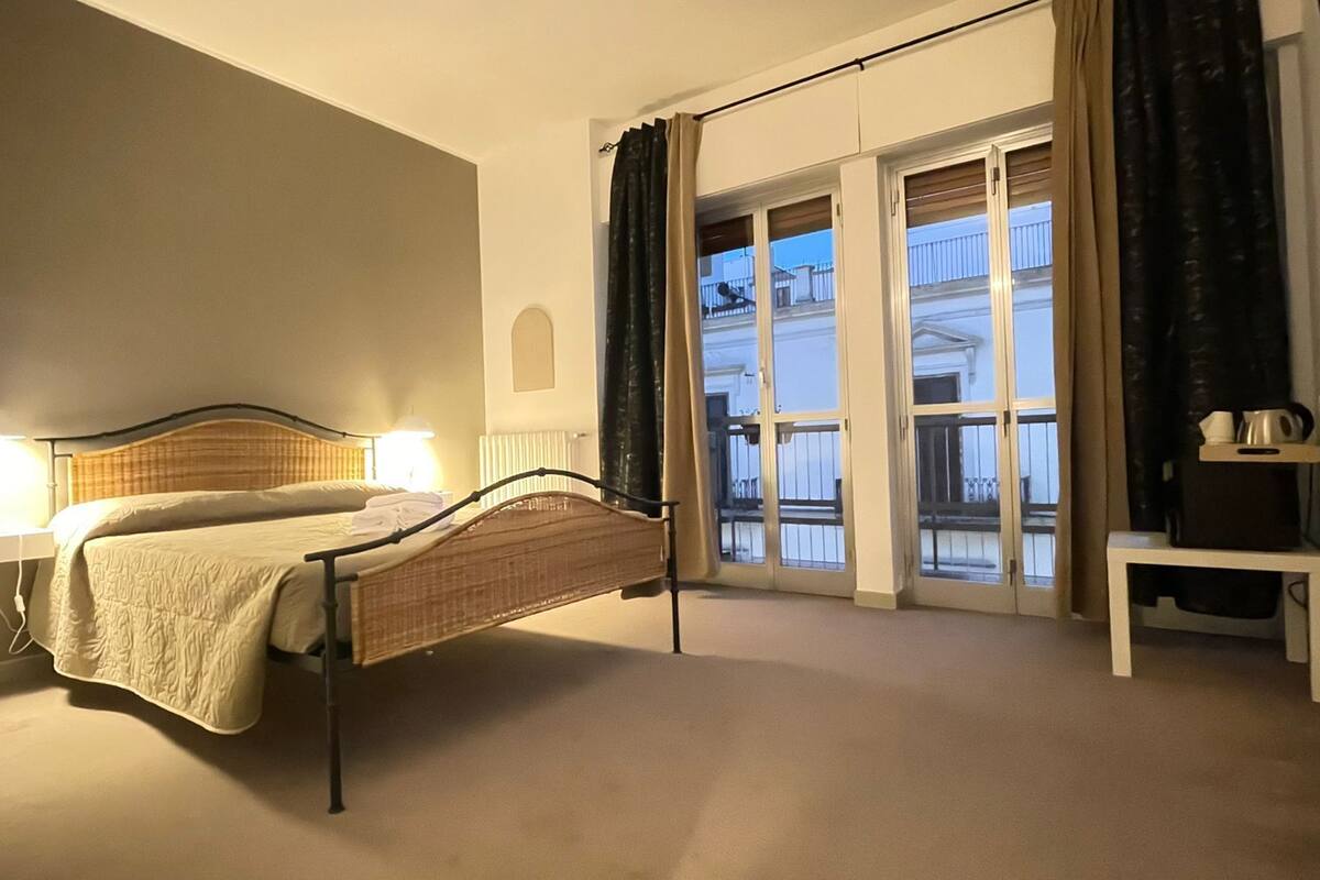 A bedroom with a bed, bedside lamps, a small table, and a view of the outside through a glass door.