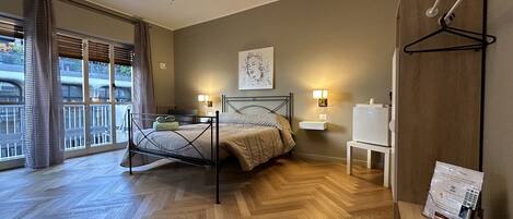 A bedroom with a bed, bedside lamps, a wooden floor, a view of the outside, and a hanging coat rack.