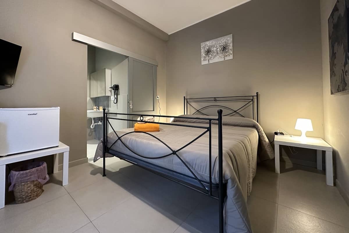A bedroom with a bed, bedside table, lamp, and a TV on a stand.